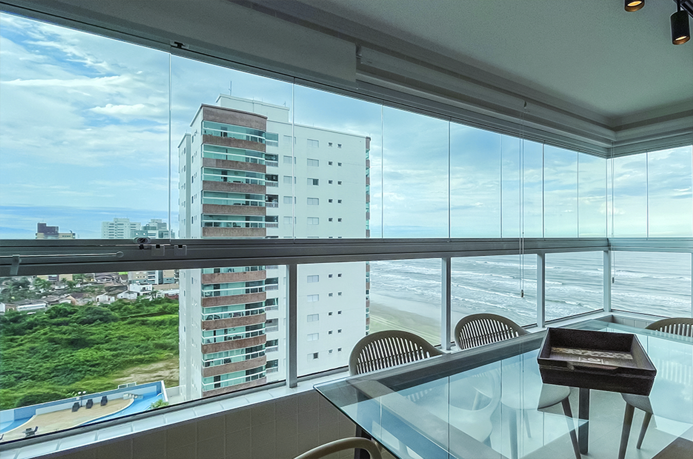 Sacada envidraçada de apartamento de alto padrão com vista panorâmica para o mar e skyline moderno.
