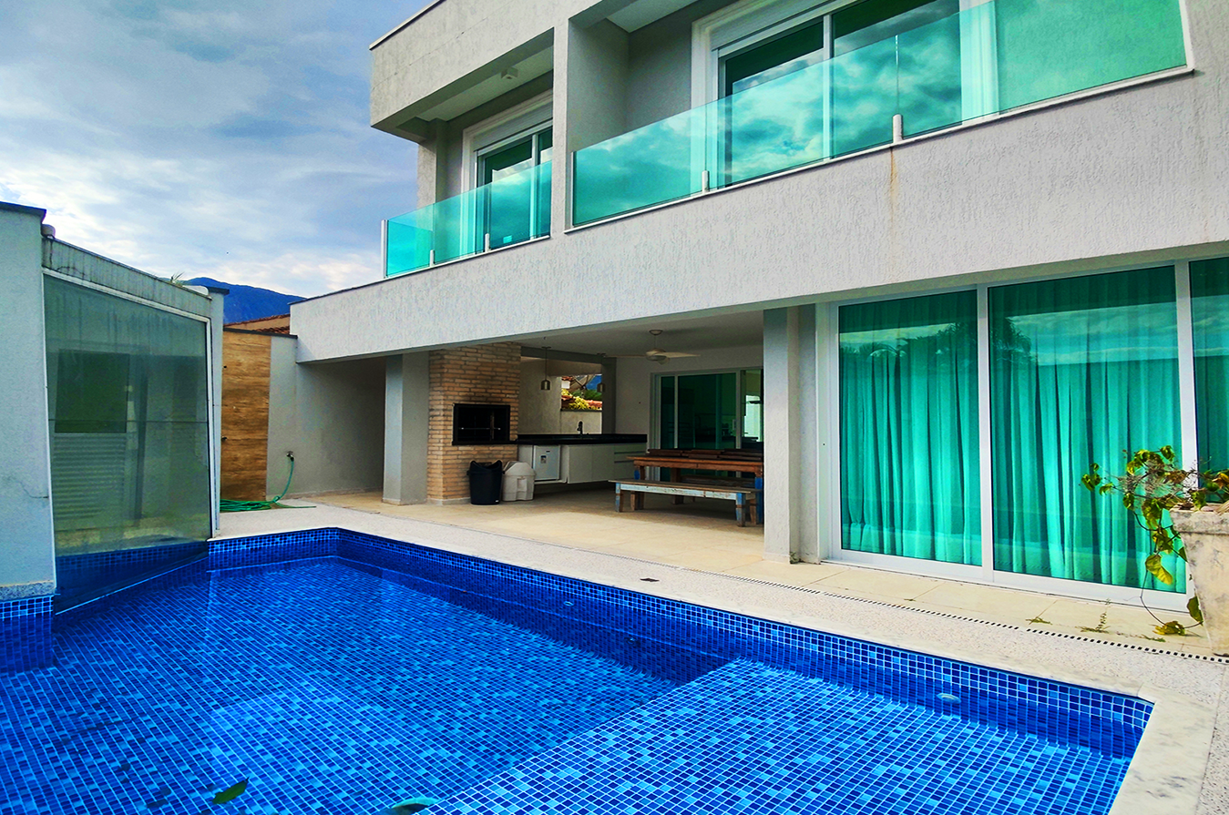 Área externa de casa de alto padrão com piscina em porcelanato azul, sacada envidraçada e espaço gourmet integrado.