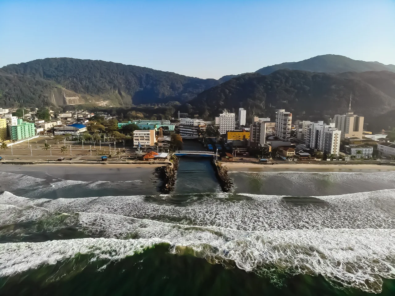 Vista aérea de Mongaguá mostrando a foz do rio, a orla e os prédios residenciais entre as encostas da Serra do Mar