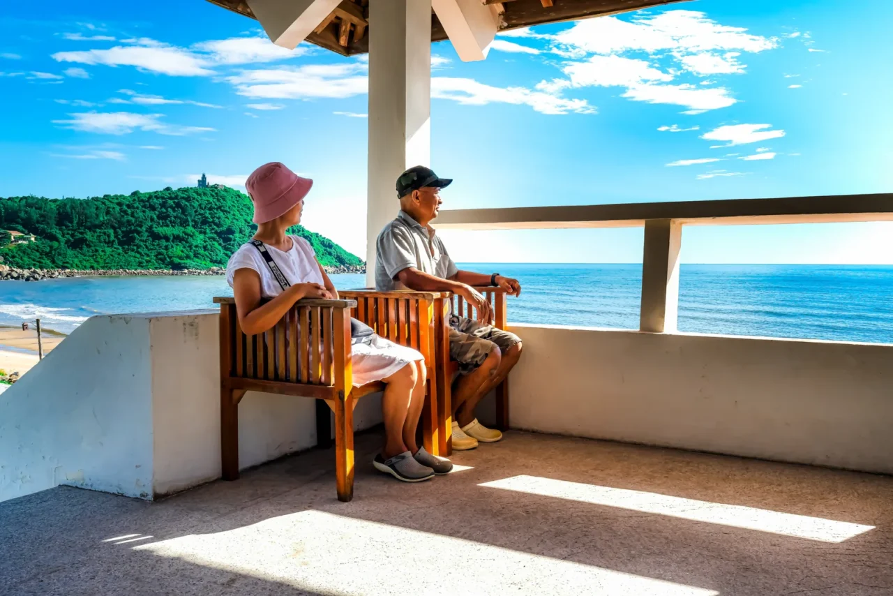 Casal maduro observando o mar de um terraço — perfil de comprador 55+ que busca wellness imobiliário
