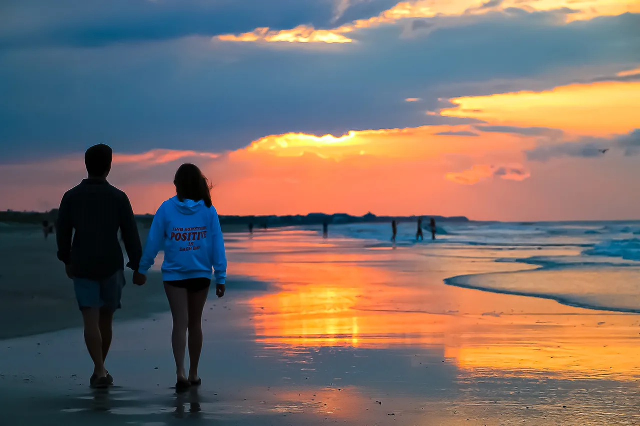 Casal caminhando na praia de Mongaguá ao entardecer, com a orla ao fundo